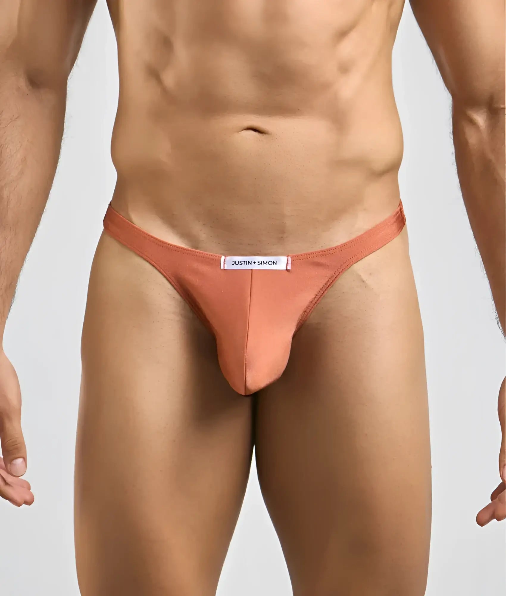 Justin Simon classic tanga in peach color made of smooth form-fitting fabric with minimalist design and branded waistband