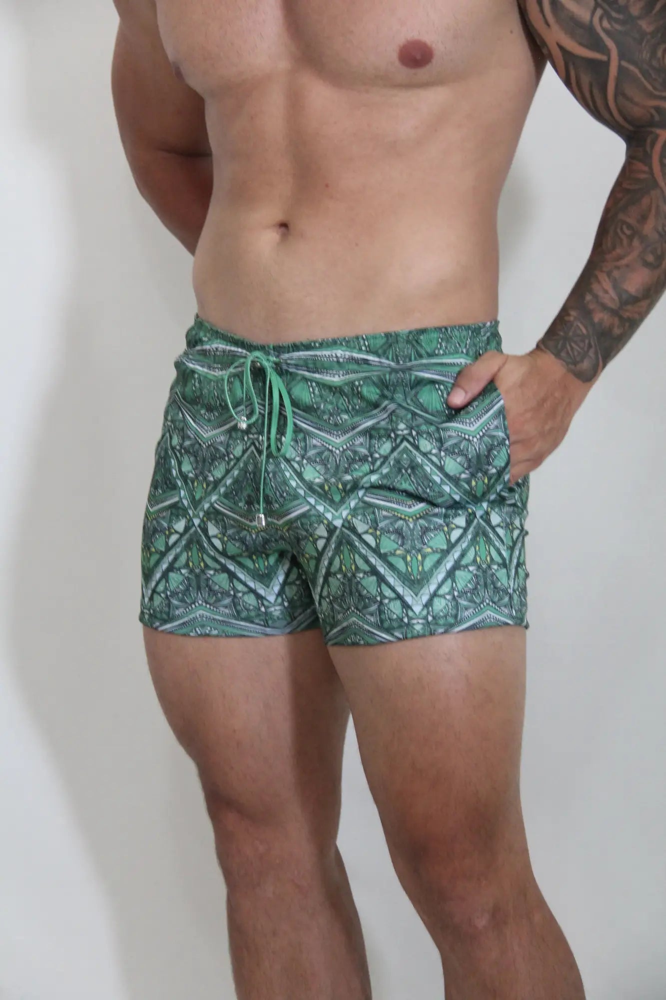 Green patterned kaleidoscope shorts with geometric design and matching drawstring swim trunks for beachwear