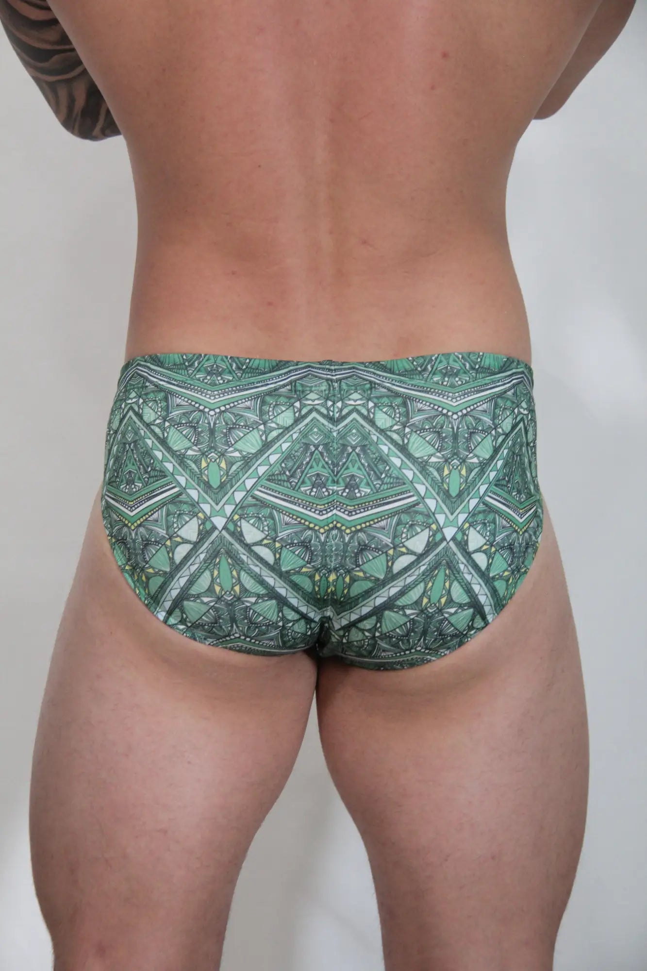 Green patterned kaleidoscope swim brief with geometric and tribal-inspired designs for casual beachwear use