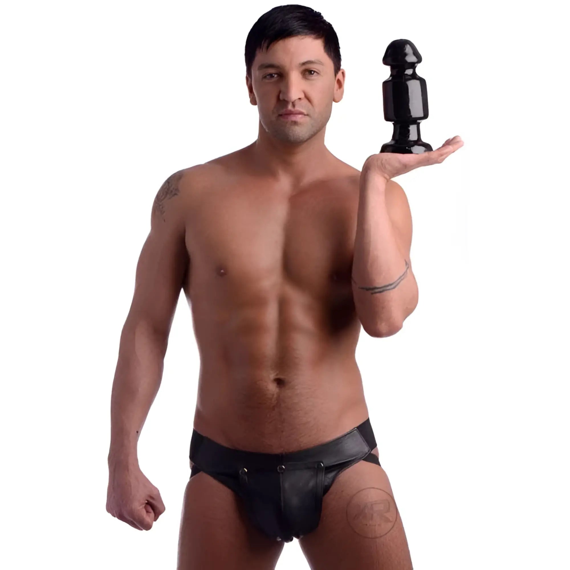 A man shirtless and wearing a leather jockstrap, holding a black Kink Industries The Keg butt plug in his open palm.