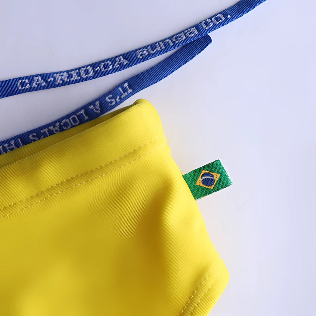 Bright yellow fabric pouch with a green and blue Brazilian flag tag for lemonade yellow mens swimming sunga beachwear