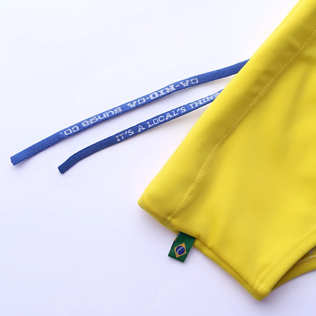 Lemonade yellow solid men’s swimming sunga with blue drawstrings white text and green brazilian flag tag for beachwear