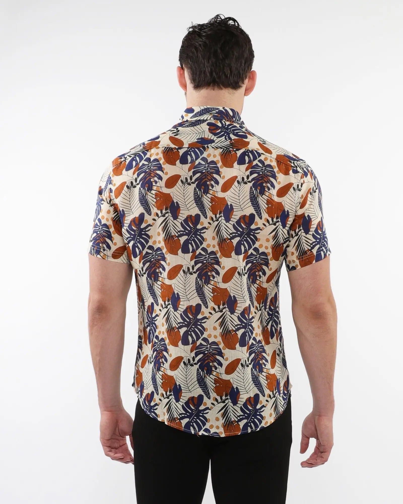 A man wearing a lightweight linen tencel short-sleeved shirt with vibrant tropical leaf and fruit pattern on light beige
