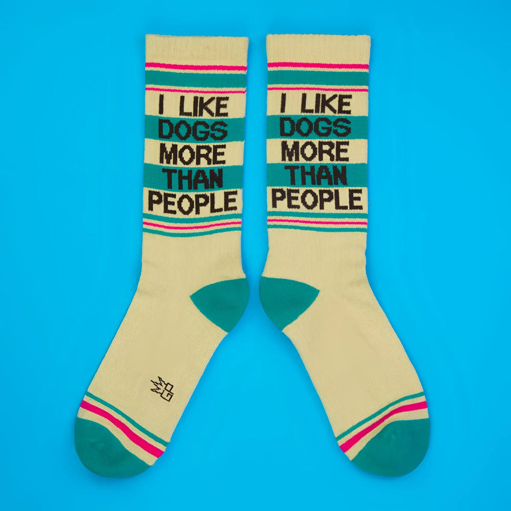 Cream-colored crew socks with teal and pink stripes and black text saying i like dogs more than people