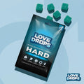 Love Drops Hard sexual enhancement gummy pouch with six sugar-coated, teal-colored square gummies on a blue background.