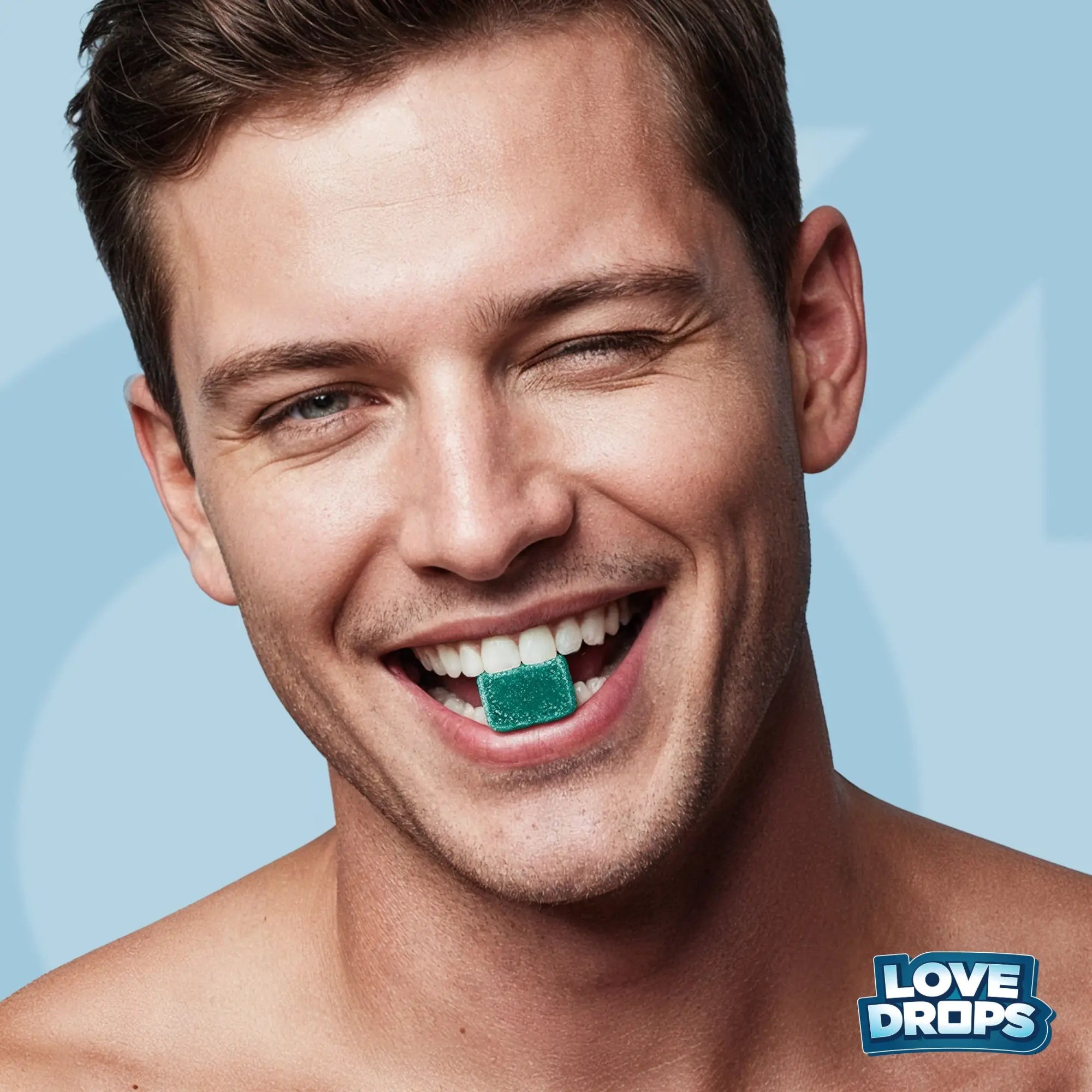 Smiling man winking while holding a green Love Drops sexual enhancement gummy in his teeth against a blue background.