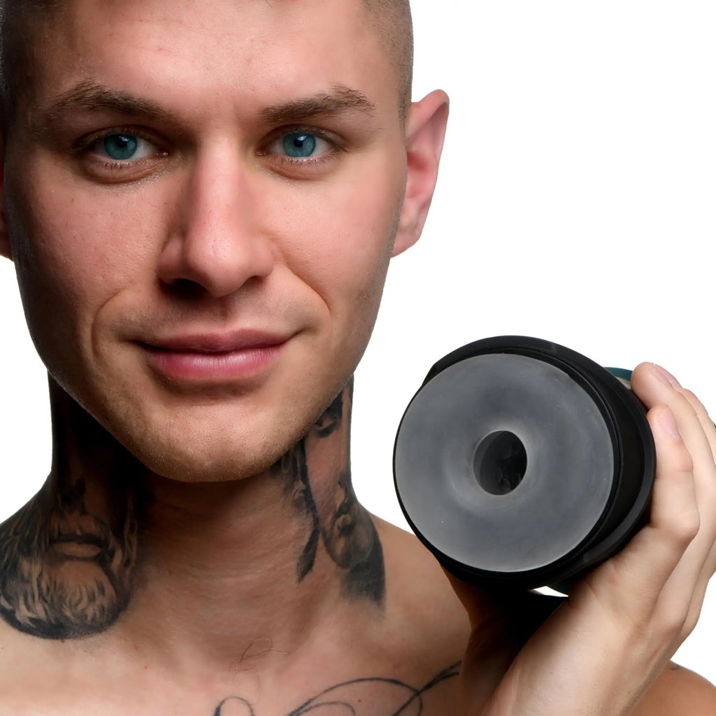 Tattooed man holds a black LoveBotz The Milker Intense 13X sucking masturbator with a circular opening.