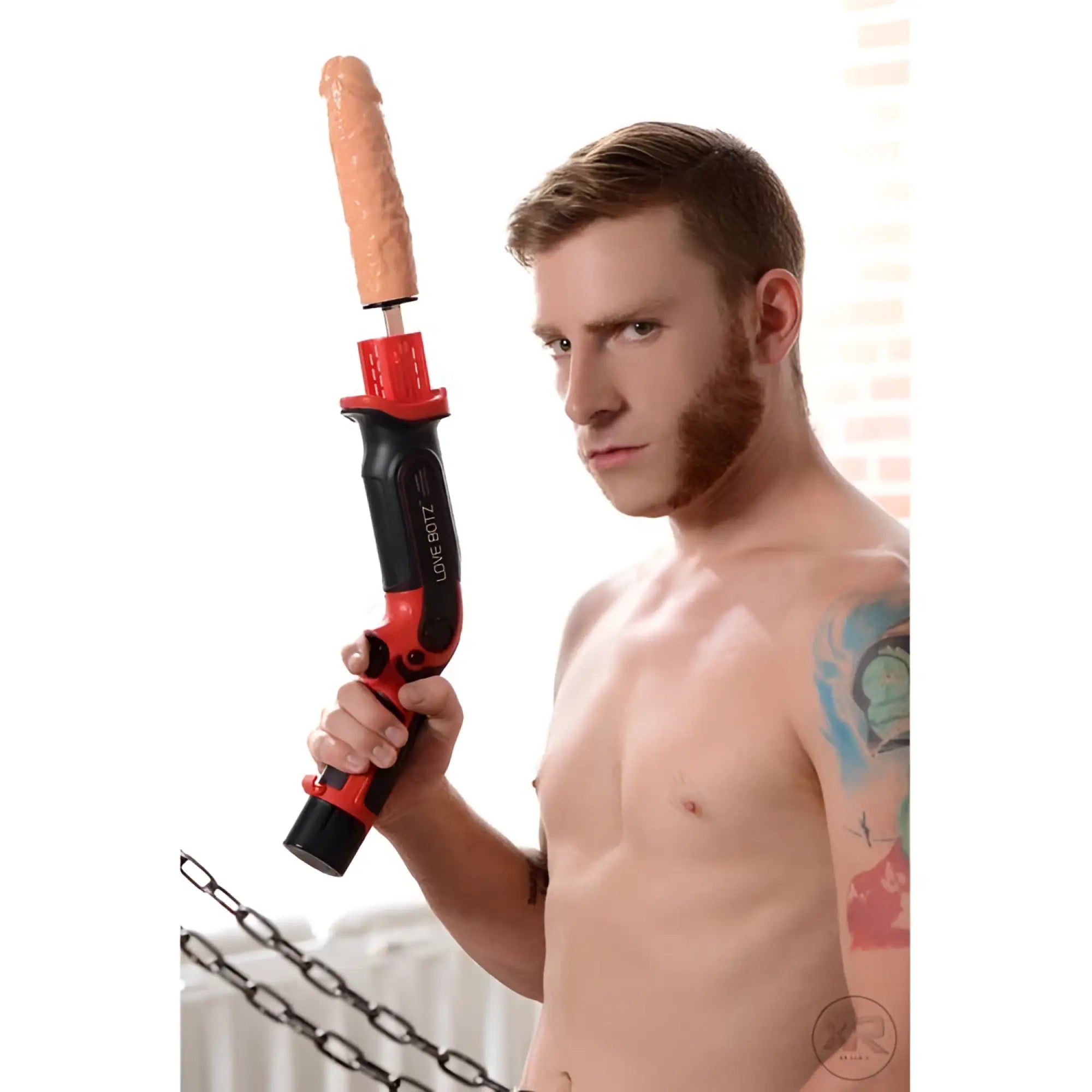 LoveBotz Thrust-Bot handheld sex machine in red and black, held by a shirtless man with arm tattoos.