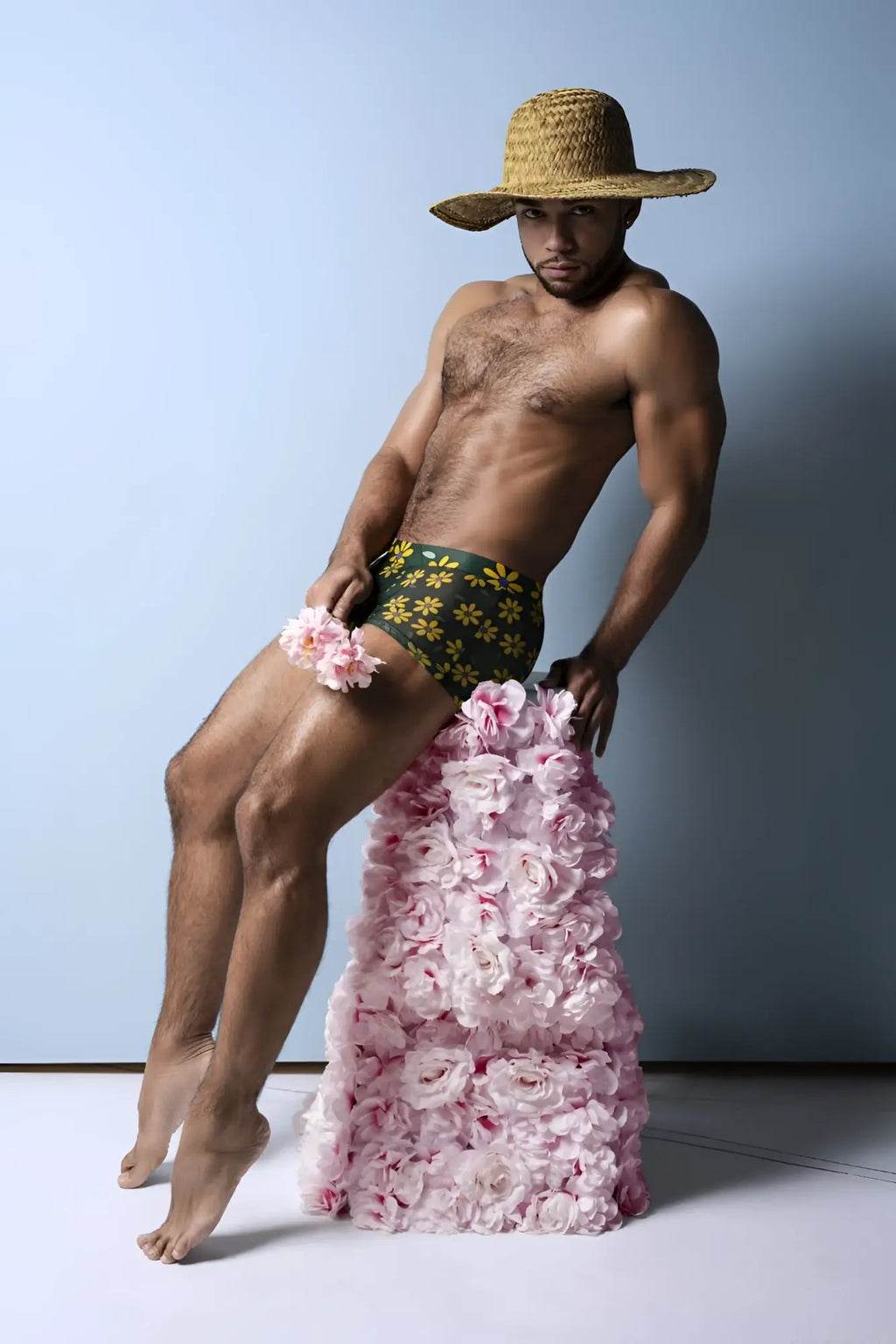 A man wearing male power daisy print petal power pouch shorts in green with pink roses cascading down his legs