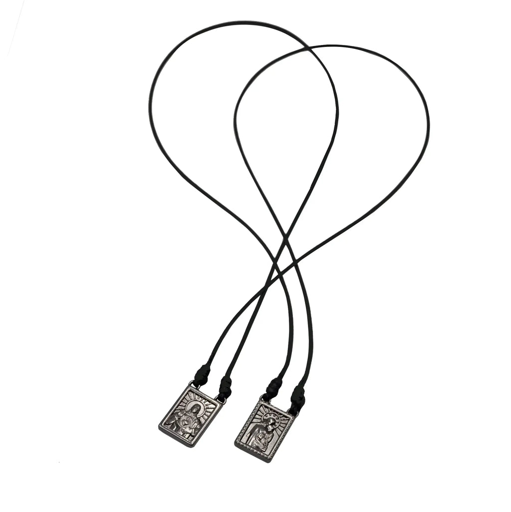 Black corded male scapular necklace with rectangular silver-toned pendant featuring engraved religious imagery