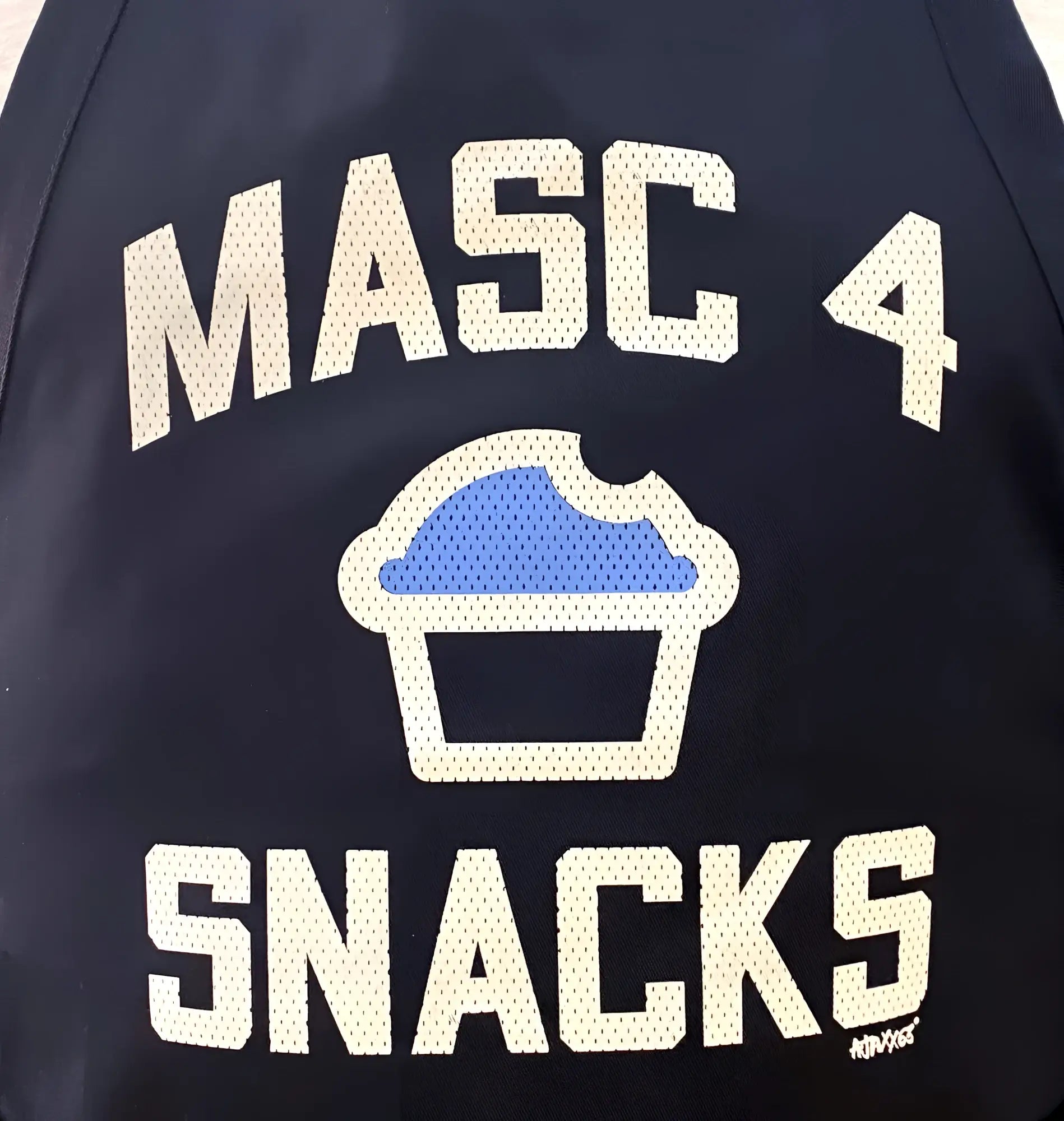 Dark navy bomber jacket with white mesh lettering and a blue cupcake graphic from masc4snacks apron collection