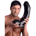 A shirtless man holding a large, black, XXXL Master Cock The Annihilator dildo against a white background.