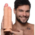 A smiling man holds a tan, realistic 10-inch Master Cock Double Stuffer dildo with prominent veins against a white background.
