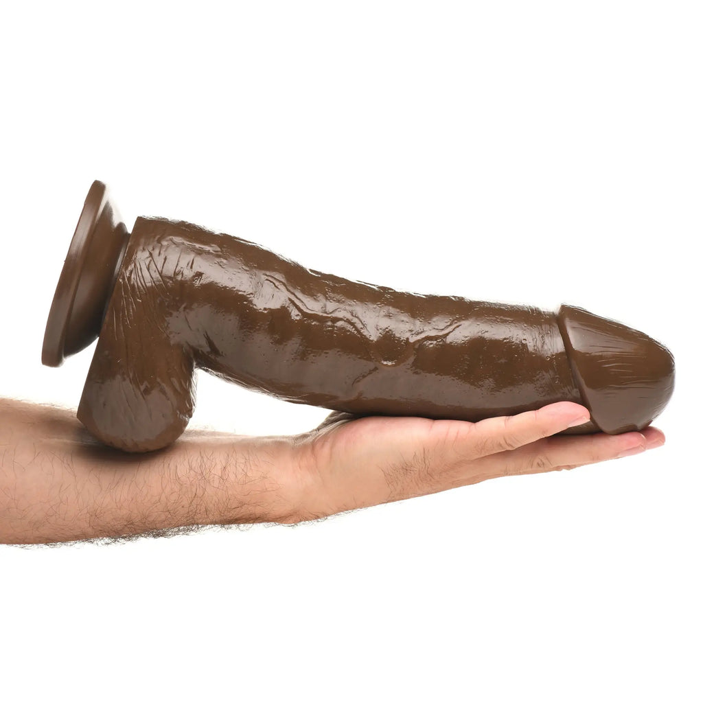 Master Cock Forearm dildo in dark brown, featuring realistic texture and a large suction cup base, held in a hand.
