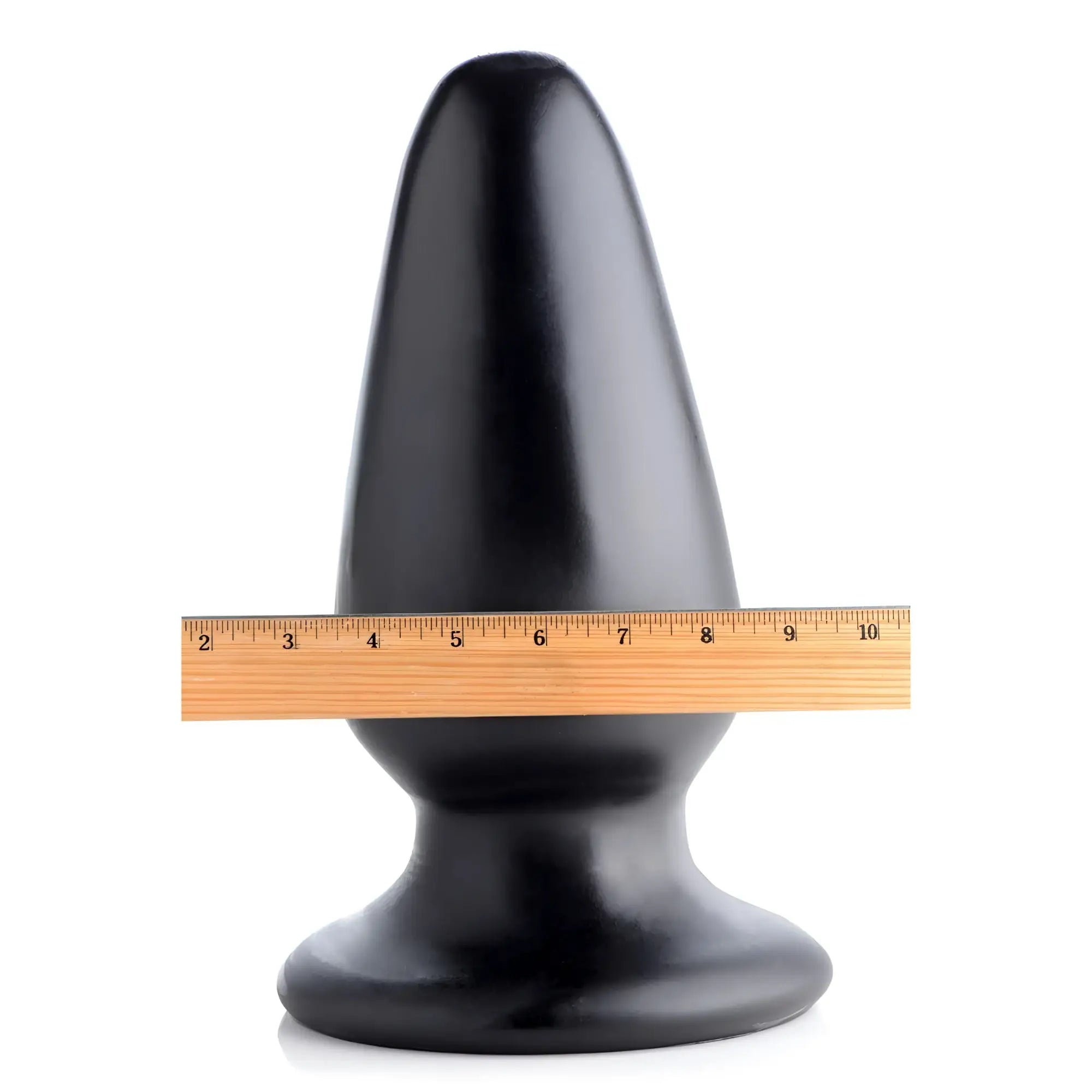 Master Cock Gigantor XXXL black tapered butt plug standing behind a wooden ruler for scale on a white background.