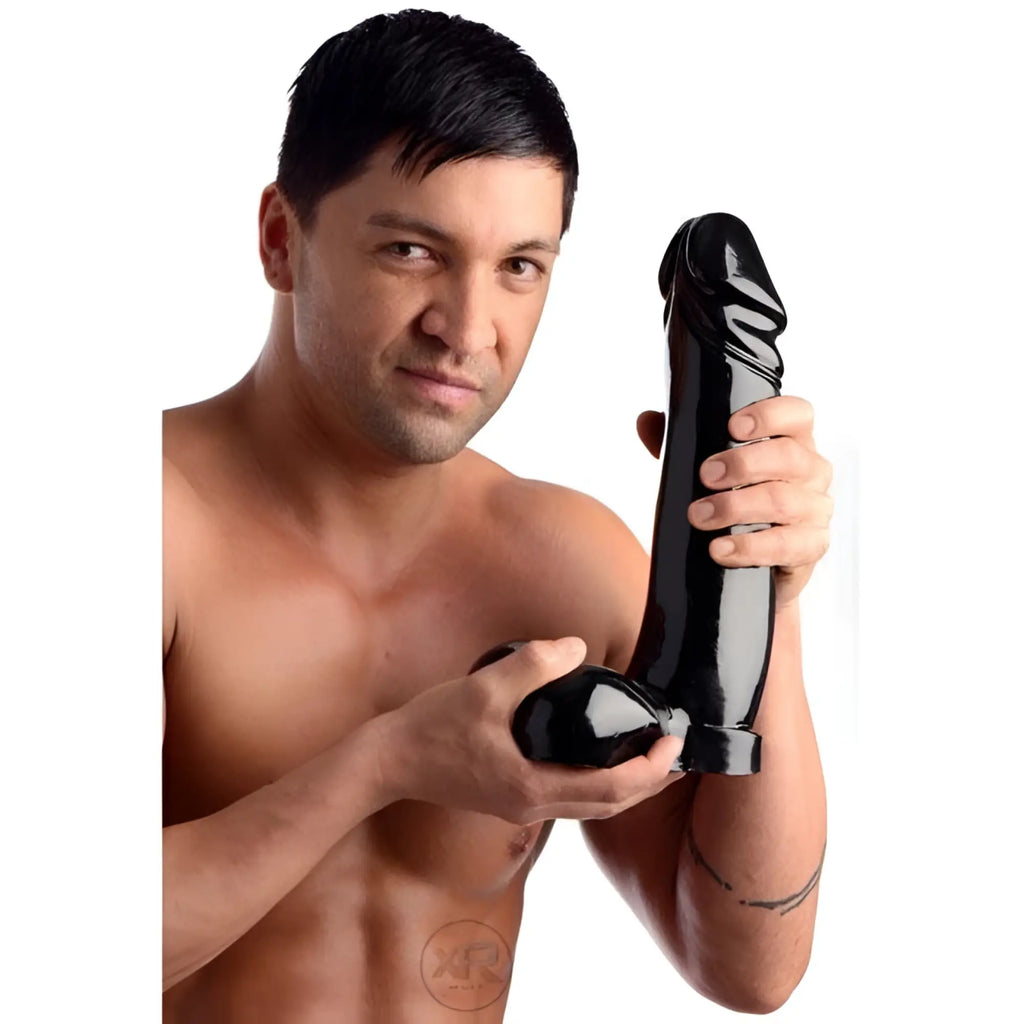A shirtless man holding a large, black Master Cock The Immense Ivan dildo with realistic detailing.