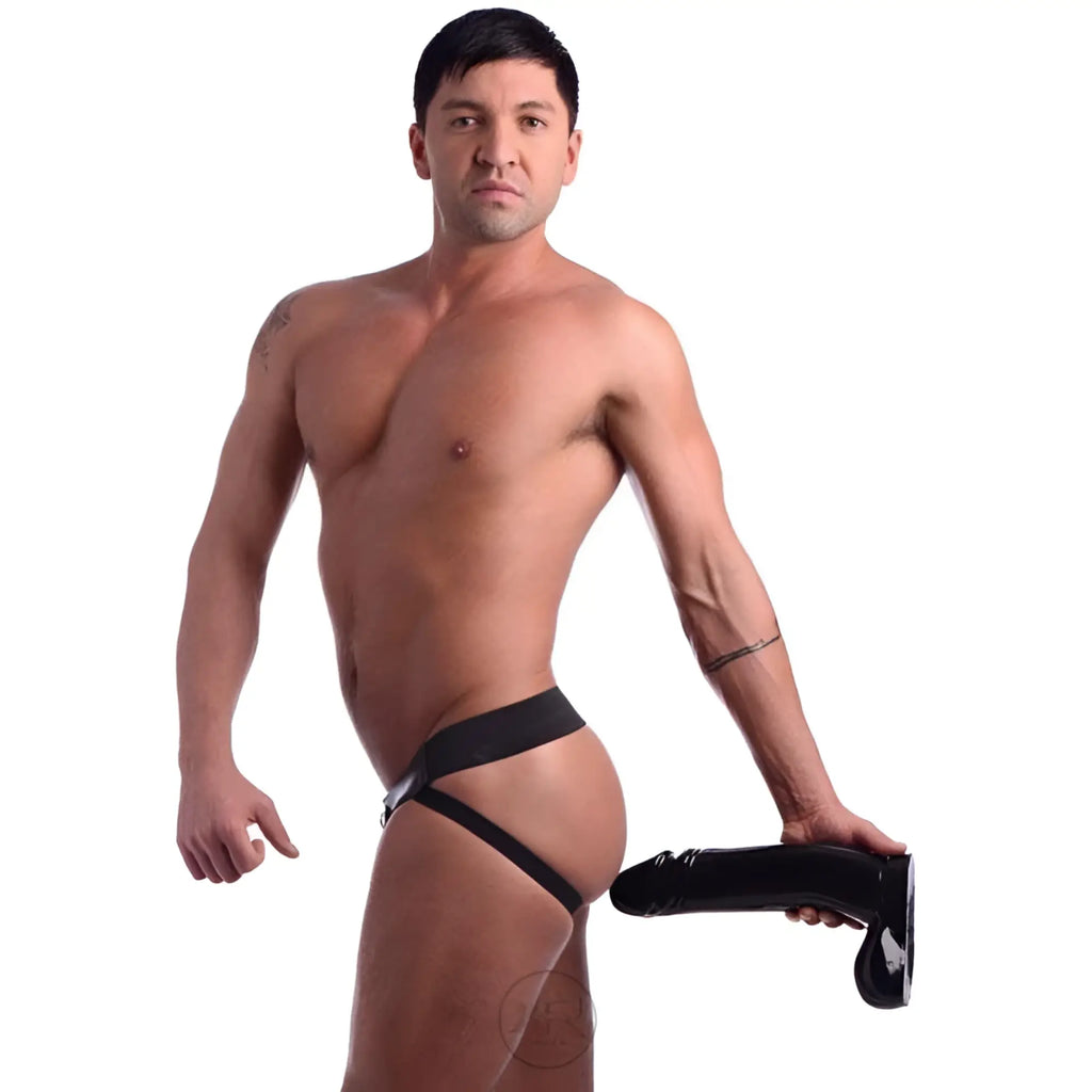 A muscular man wearing a black jockstrap harness holding a large, black Master Cock The Immense Ivan dildo.