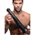 A shirtless man holding a 17-inch, black, textured Master Cock Pony Boy horse dildo against a white background.