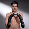 A shirtless man holds a black Master Cock The Python XL double-ended, U-shaped silicone dildo against a grey background.