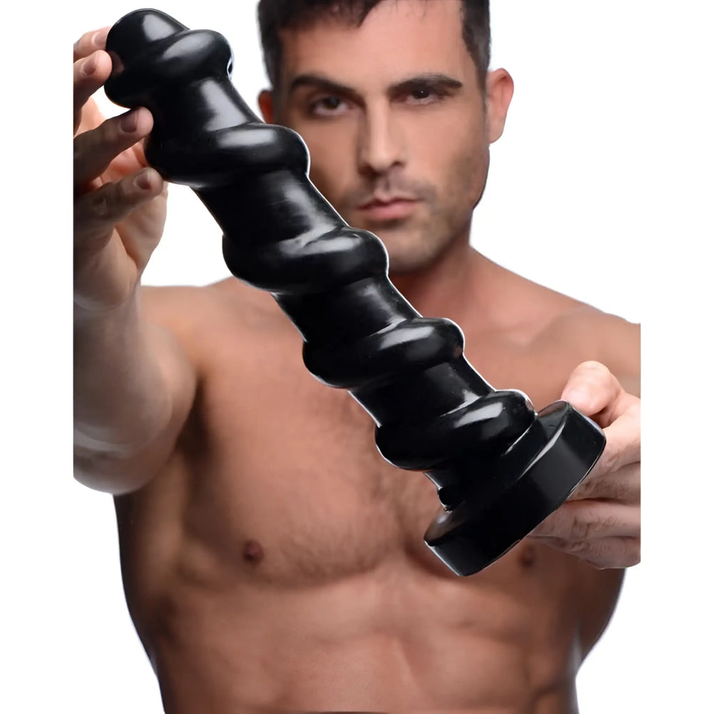 A man holds a black, spiral-shaped Master Cock Screw dildo with a flared base against a white background.