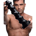A man holds a black, spiral-shaped Master Cock Screw dildo with a flared base against a white background.