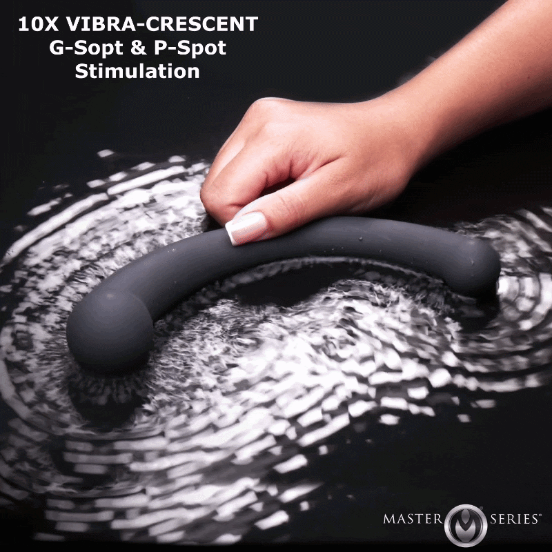 A hand holds a dark grey, curved Master Series Vibra-Crescent silicone dildo vibrating on a reflective black surface.