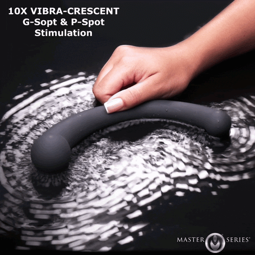 A hand holds a dark grey, curved Master Series Vibra-Crescent silicone dildo vibrating on a reflective black surface.