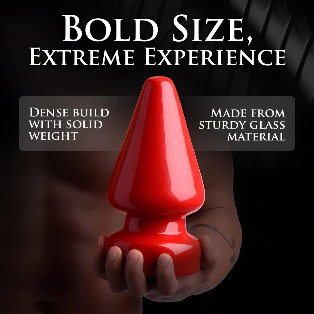Master Series The Anal Destructor, a large, glossy red glass butt plug held in a hand against a black background.