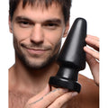 A man holding a large, matte black Master Series Ass Max anal plug against a white background.