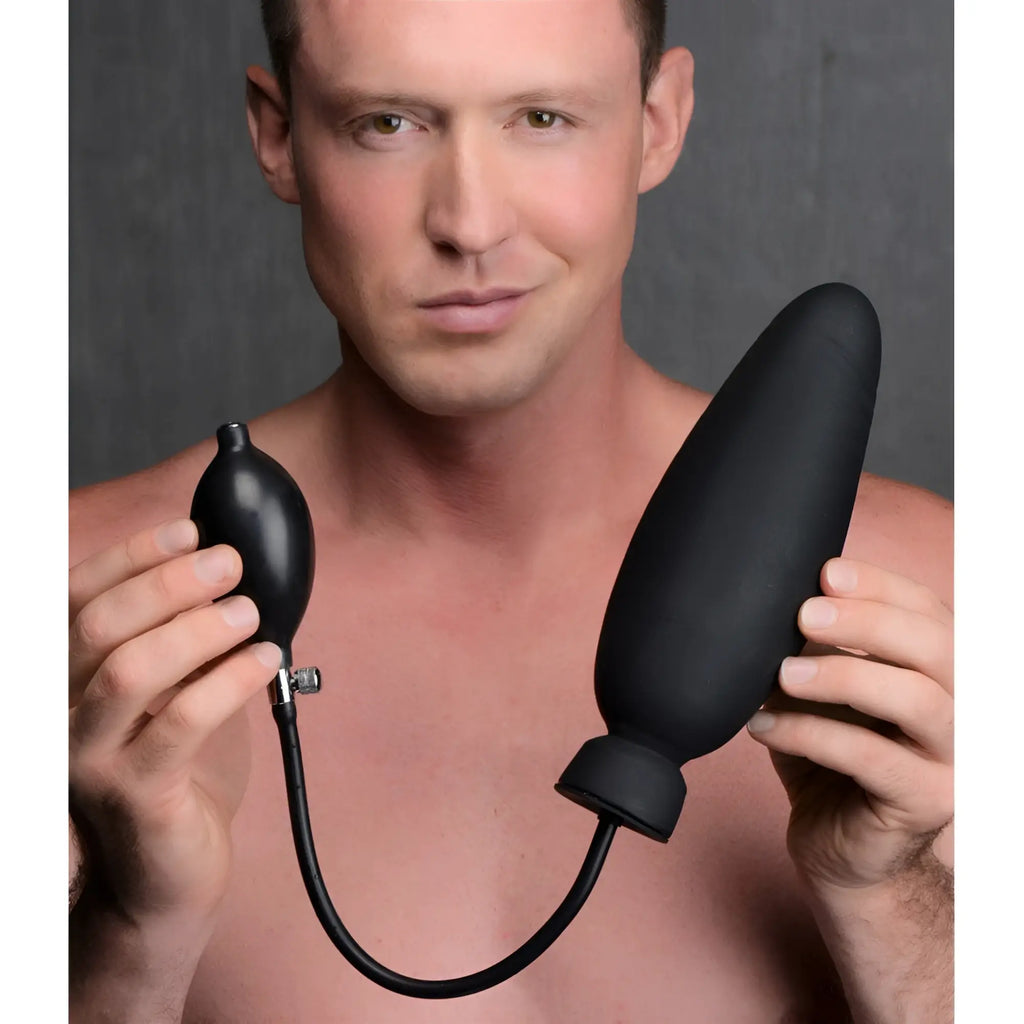 A man holds a black Master Series Ass-Pand inflatable silicone dildo, featuring a hand pump and bulb.