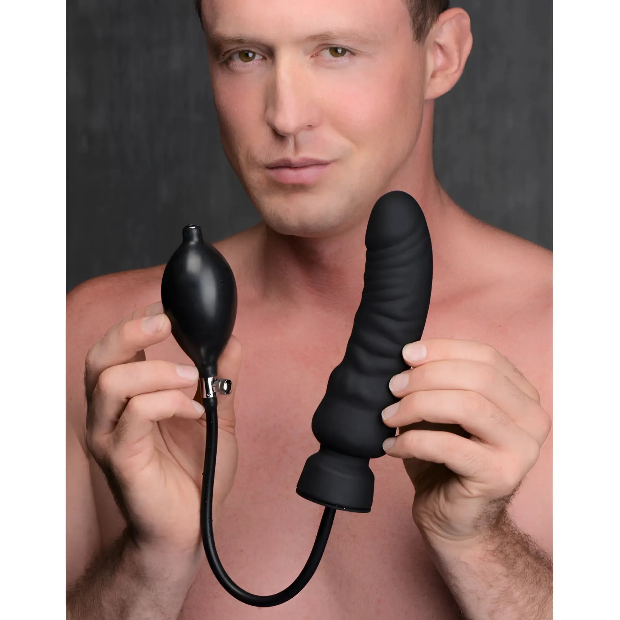 A shirtless man holding a black, ribbed Master Series Ass-Pand inflatable silicone dildo with an attached hand pump.
