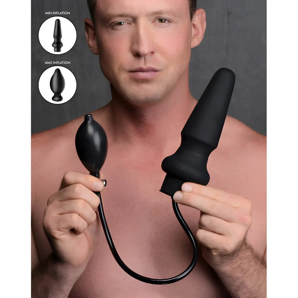 Master Series Ass-Pand inflatable black silicone anal plug held by a man, showing min and max inflation levels.