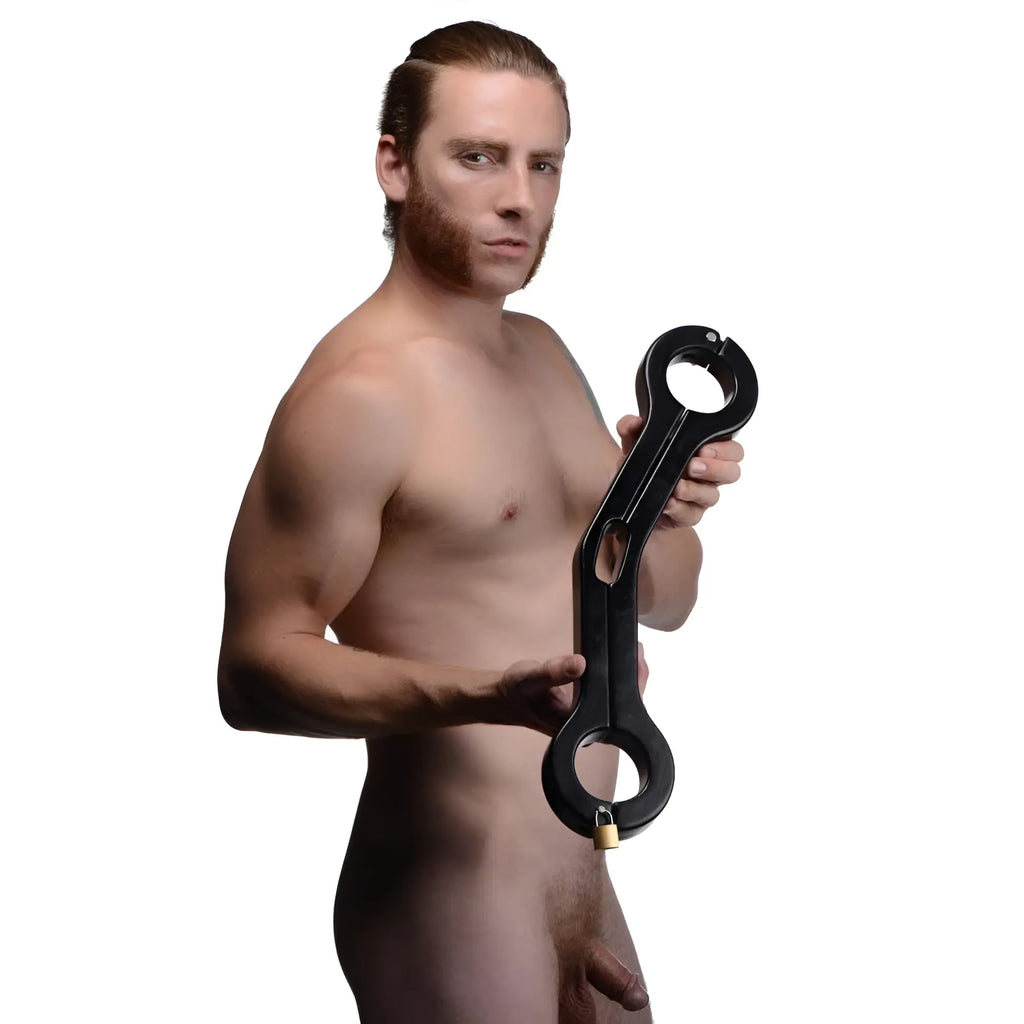 A man holding a black, heavy-duty Master Series Balls to Wrist Humbler restraint with a gold padlock.