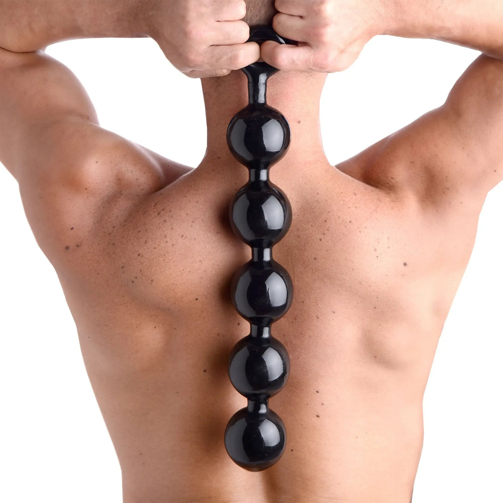 Master Series The Black Baller: a person holds a vertical row of five large, glossy black spherical anal beads.