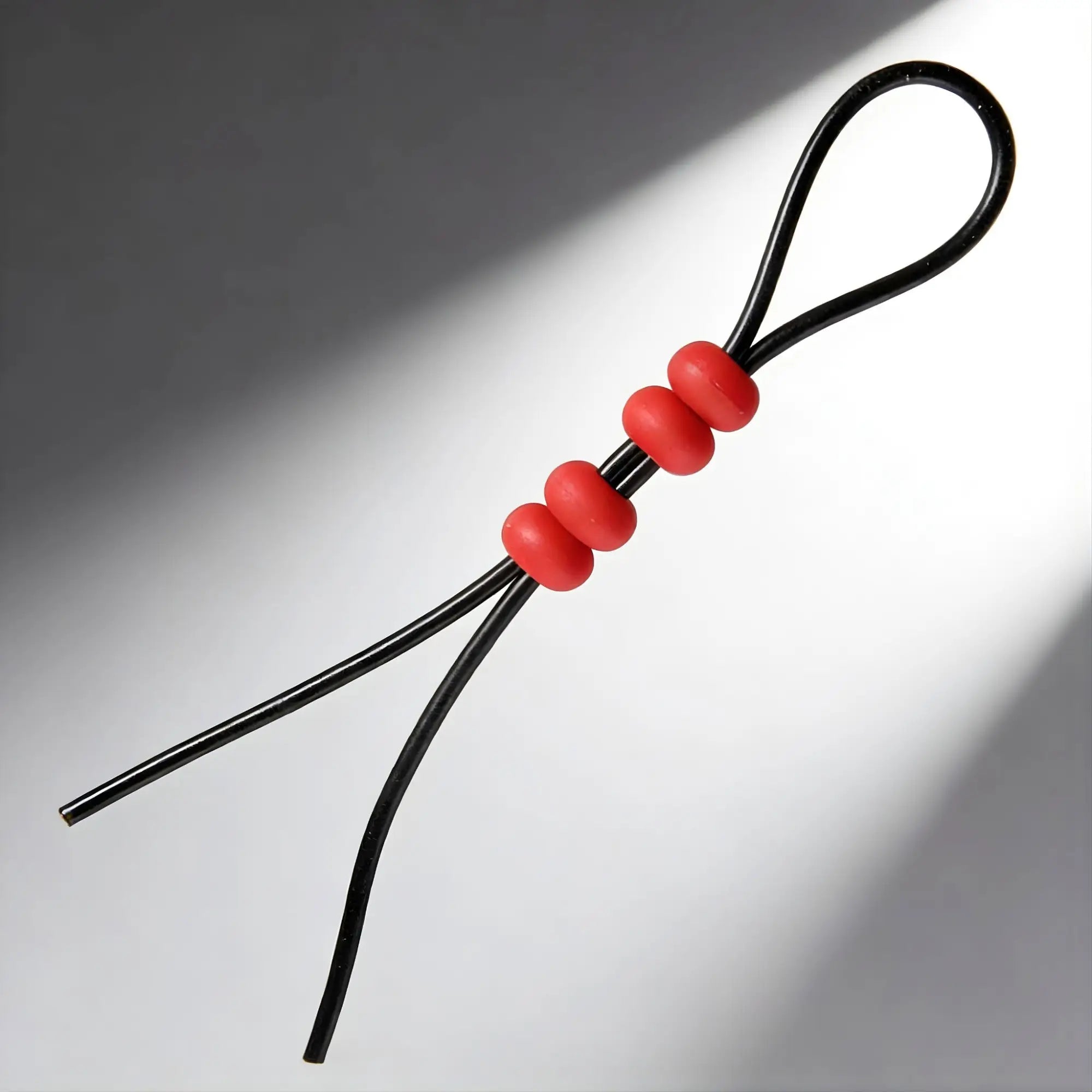 Master Series Bolo Lasso cock ring: a flexible black cord with two red sliding beads for adjustable sizing.
