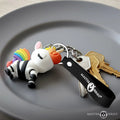 Master Series Bondage Unicorn keychain with rainbow mane, black straps, and silver hardware on a gray plate with keys.