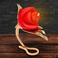 Master Series Burning Passion rose candle in a sleek, gold-colored leaf-shaped metal holder on a wooden surface.