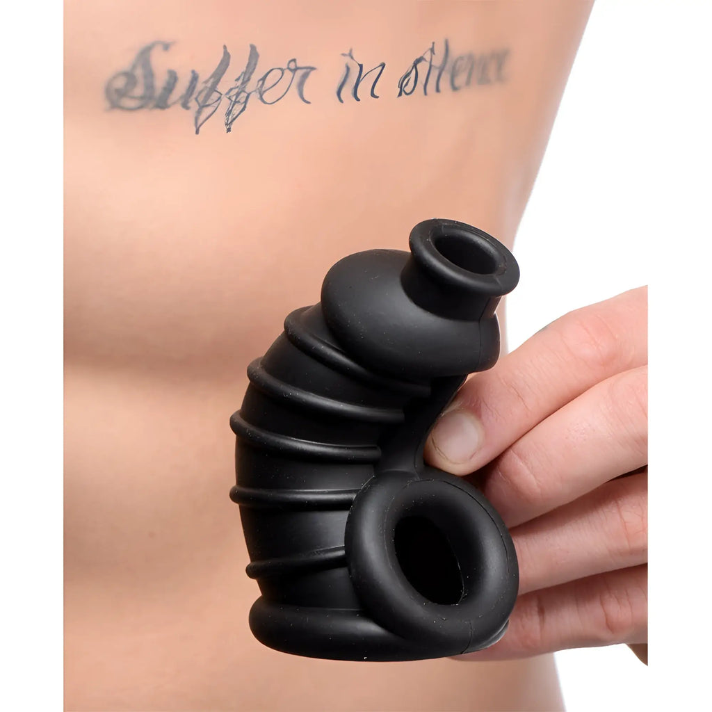 Hand holding a black, ribbed, flexible silicone Master Series The Chamber chastity cage against a tattooed torso.