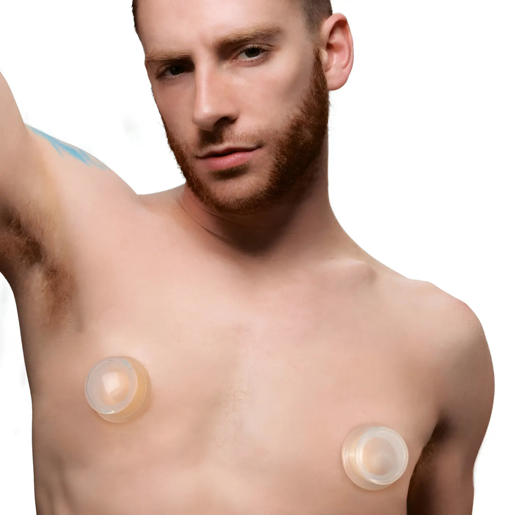 Man wearing two transparent silicone Master Series nipple suckers on his chest against a white background.