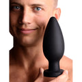 A man holds a smooth, black silicone Master Series Colossus XXL suction cup plug in front of his face.