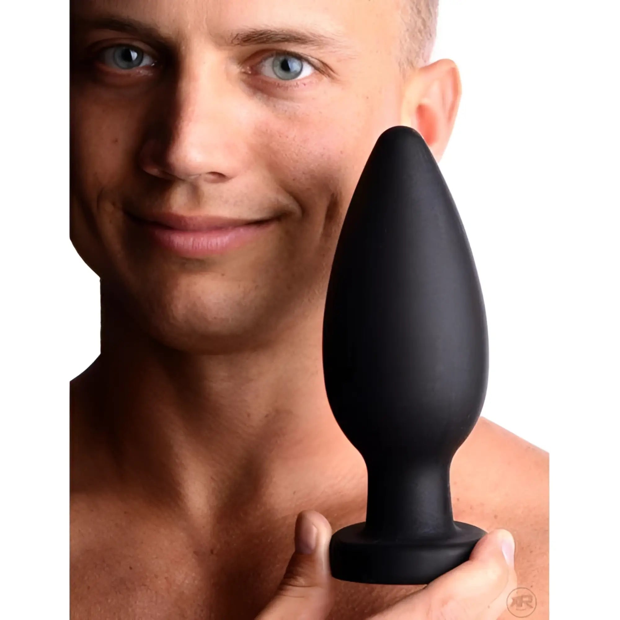 A man holds a smooth, black silicone Master Series Colossus XXL suction cup plug in front of his face.