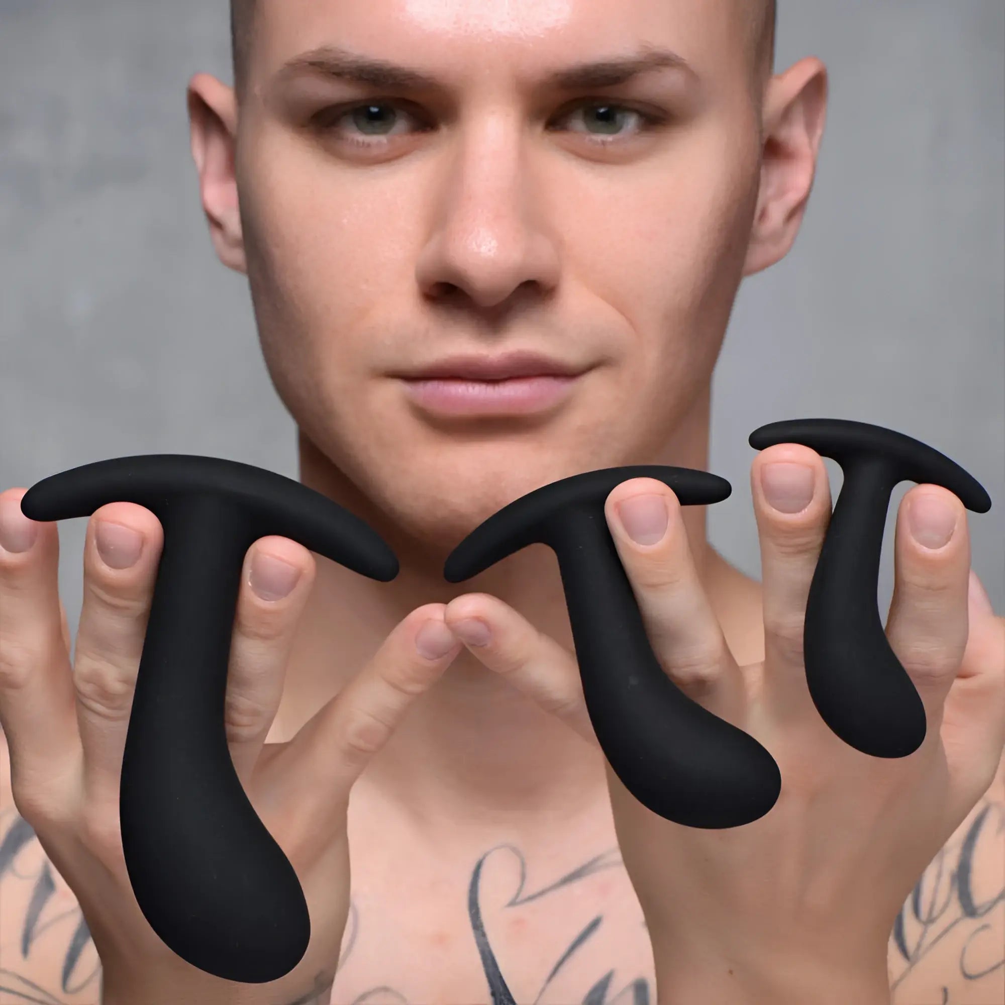 A man holding three black, curved silicone Master Series Dark Delights anal trainers of different sizes.