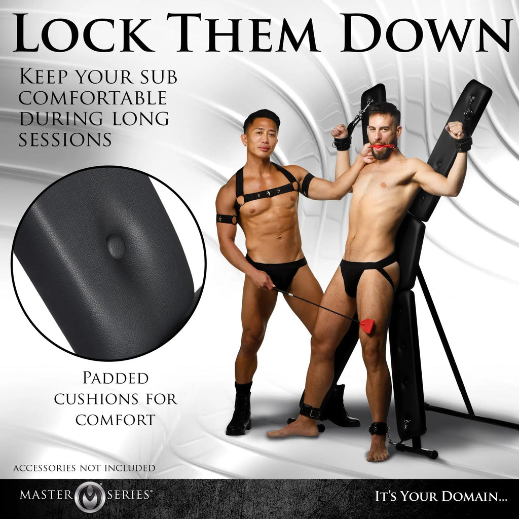 Master Series Deluxe St. Andrew's Cross: A black, padded X-frame restraint stand used by two men in a studio setting.