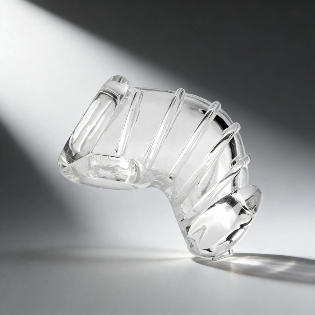 Master Series Detained Soft Body chastity cage in a clear, flexible, curved silicone design on a grey background.