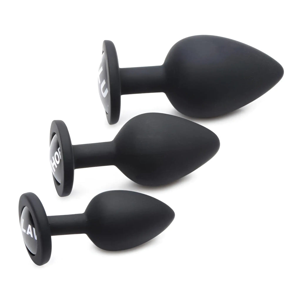Master Series Dirty Words Anal Plug Set: three matte black silicone plugs in graduating sizes with text on the bases.