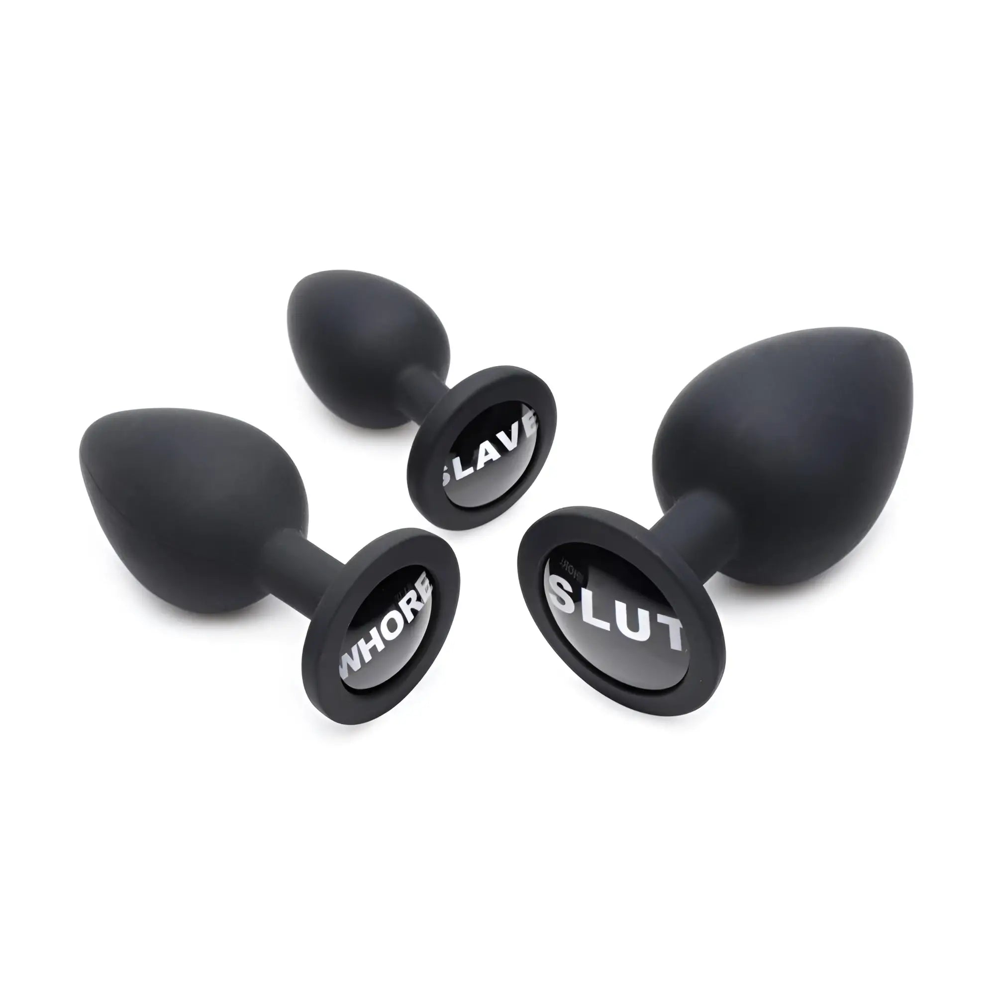 Three black Master Series Dirty Words anal plugs in varying sizes with SLAVE, WHORE, and SLUT printed on their bases.