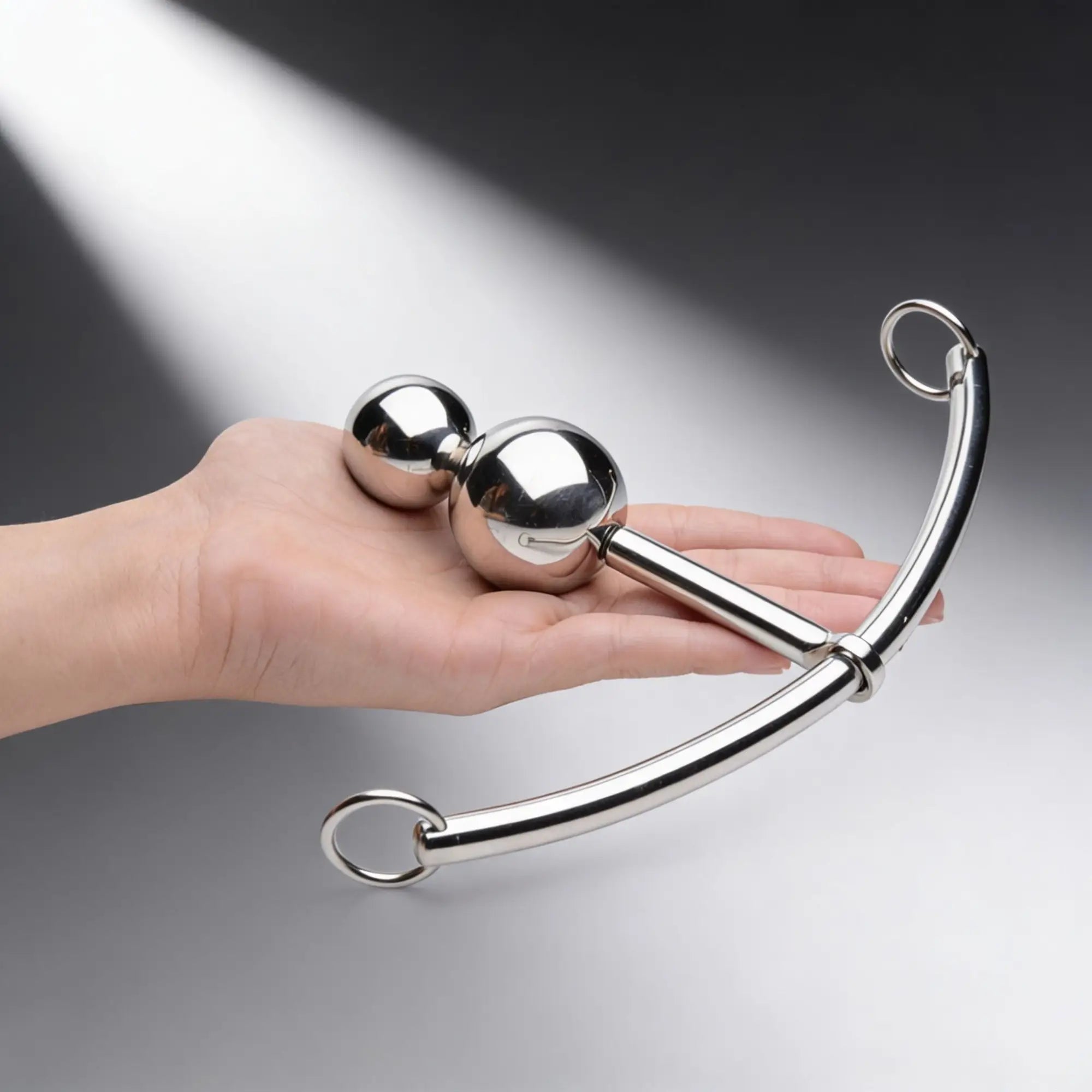 Master Series Double Ball Plug with a silver curved sliding O-ring rod, held in a hand against a grey background.