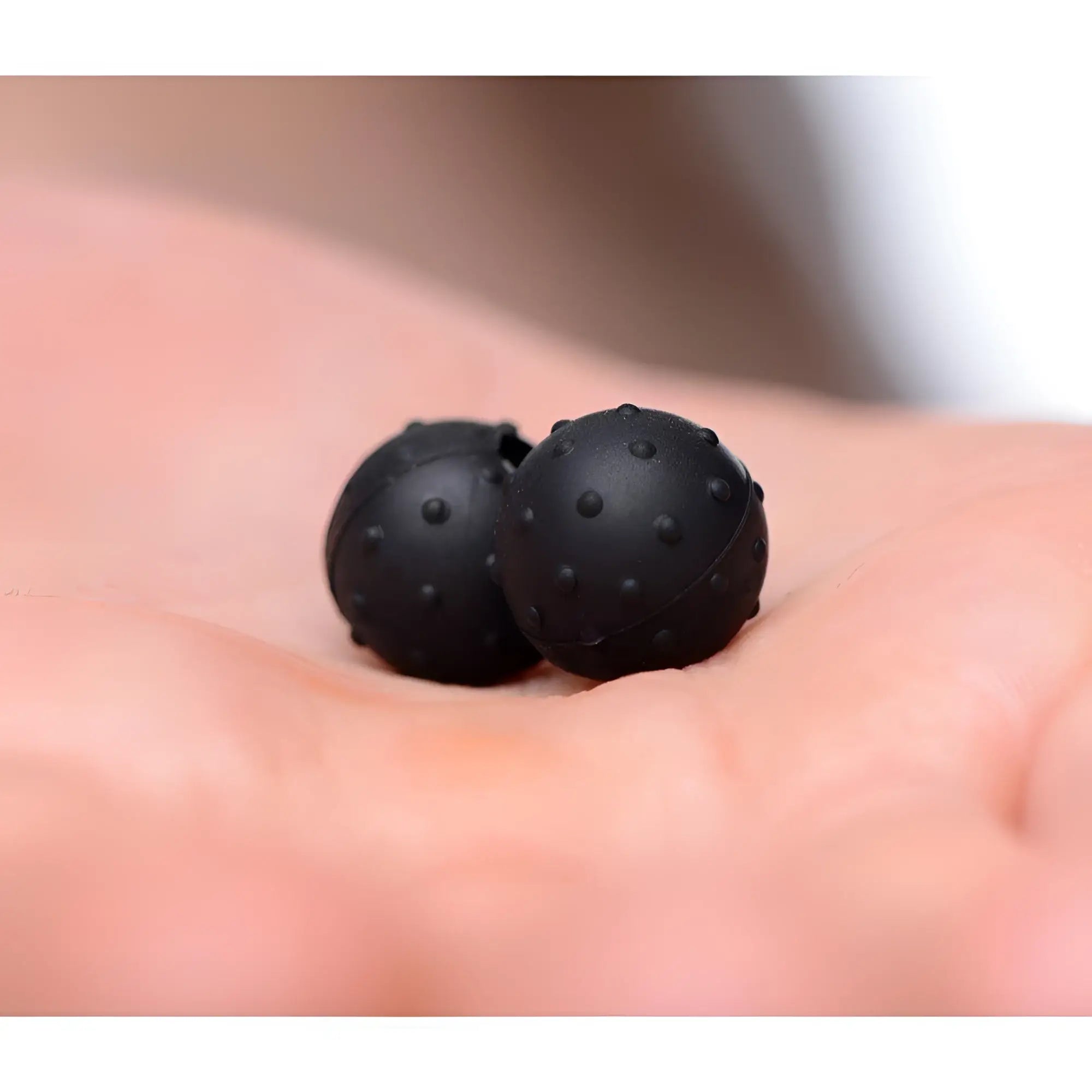 Two black, nubbed silicone Master Series Dragon's Orbs magnetic balls resting in a person's palm.