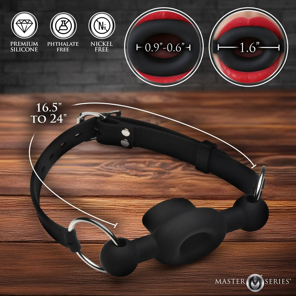 Master Series black silicone forced feeding gag on wood background, showing adjustable strap and sizing details.
