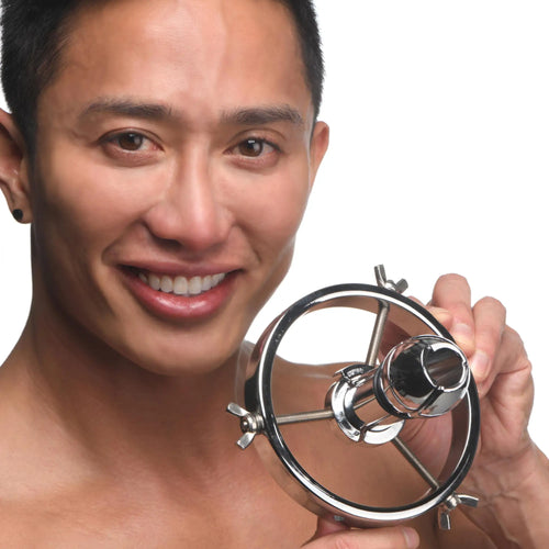 A smiling man holds a silver, stainless steel Master Series Forced Spread Anal Explorer with an adjustable ring design.